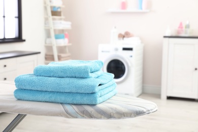 Stack of towels on ironing board against blurred background, space for text