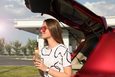Beautiful young woman with hot dog near car at gas station