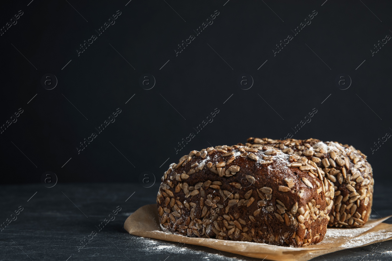 Photo of Fresh wholegrain bread on table against black background. Space for text