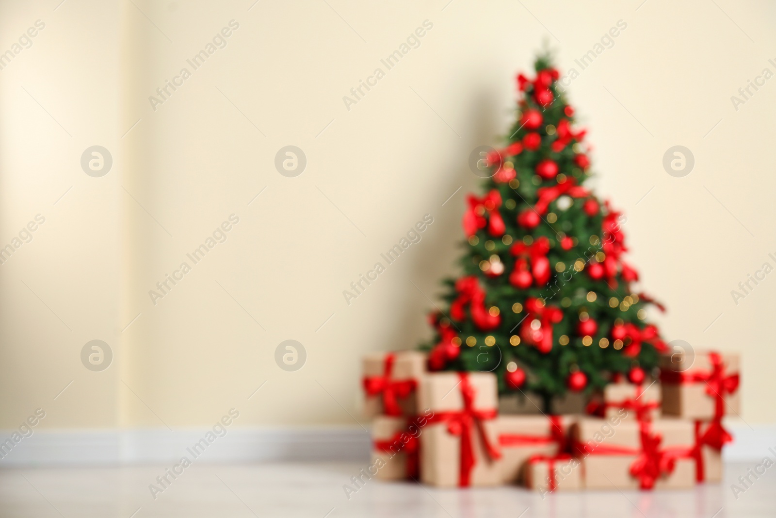 Photo of Blurred view of decorated Christmas tree and gift boxes near beige wall. Space for text
