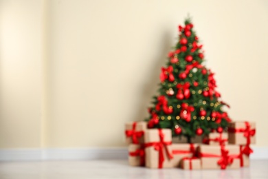 Blurred view of decorated Christmas tree and gift boxes near beige wall. Space for text