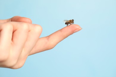 Photo of Bee going to sting woman on light blue background, closeup. Space for text