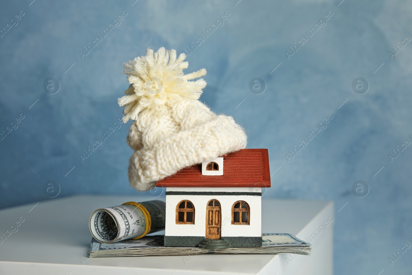 Photo of House model with warm hat and money on table against color background. Heating expenses