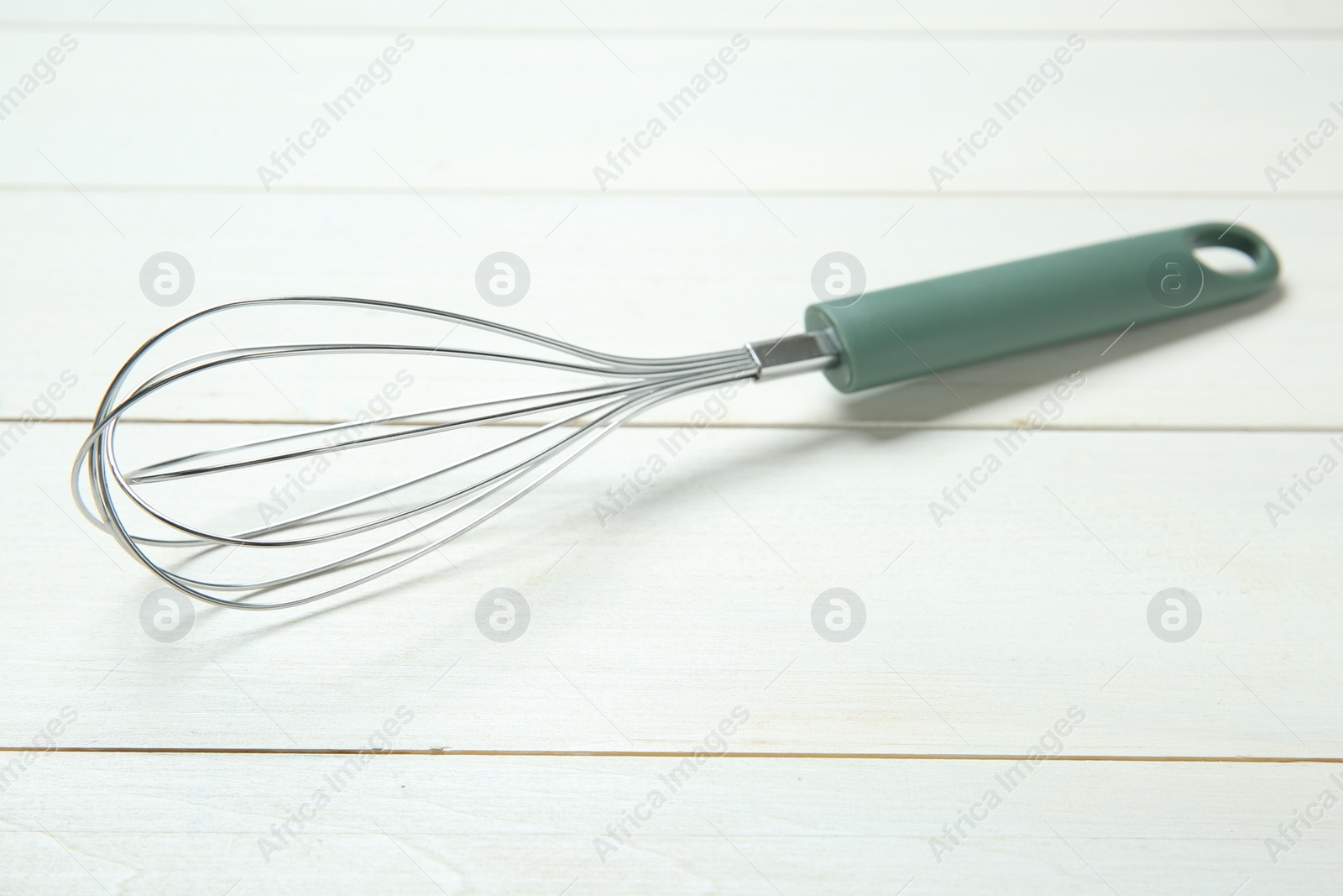Photo of One metal whisk on white wooden table