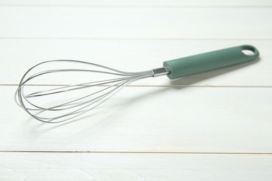 Photo of One metal whisk on white wooden table