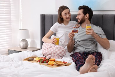 Happy couple eating tasty breakfast on bed at home