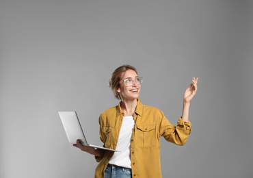 Portrait of young woman with modern laptop on grey background