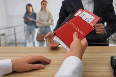 Agent giving passports with tickets to client at check-in desk in airport, closeup