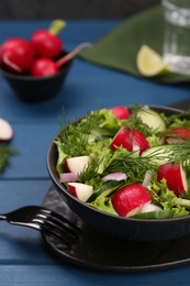 Tasty salad with radish in bowl on blue wooden table