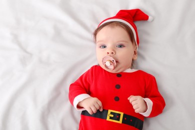 Photo of Cute baby wearing festive Christmas costume with pacifier on white bedsheet, top view