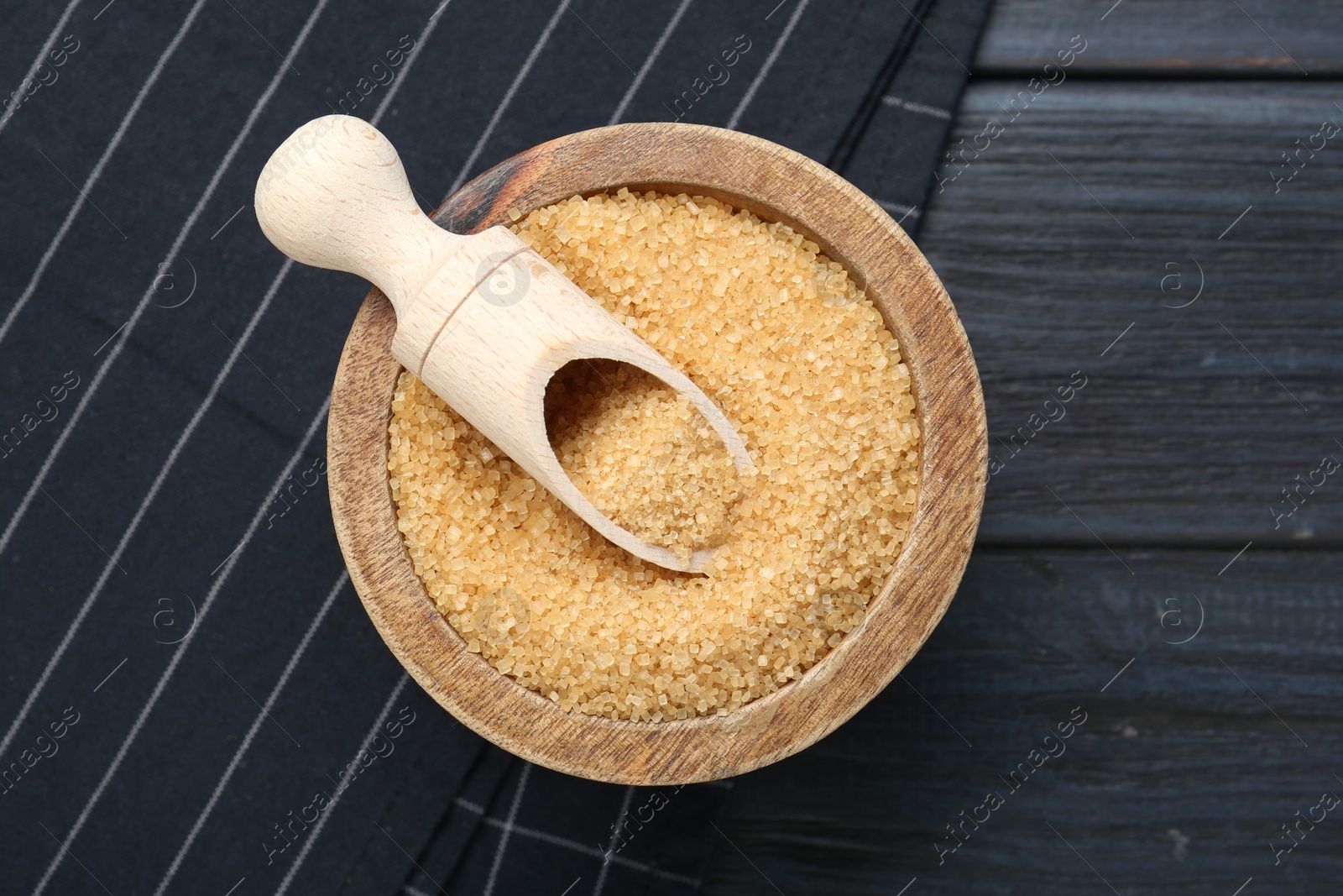 Photo of Brown sugar in bowl and scoop on black wooden table, top view