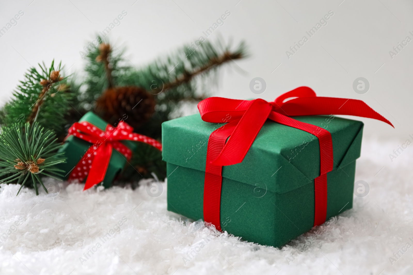 Photo of Christmas gift box with red bow and fir tree branches on snow. Space for text