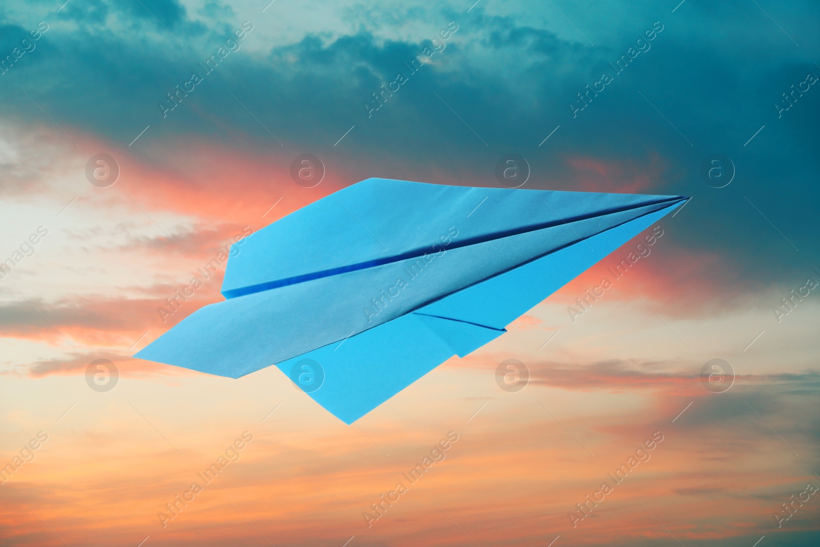 Image of Light blue paper plane and view of beautiful sky at sunset