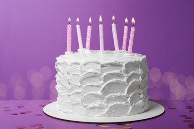 Delicious cake with cream and burning candles on purple background