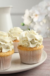 Tasty cupcakes with vanilla cream on pink wooden table, closeup