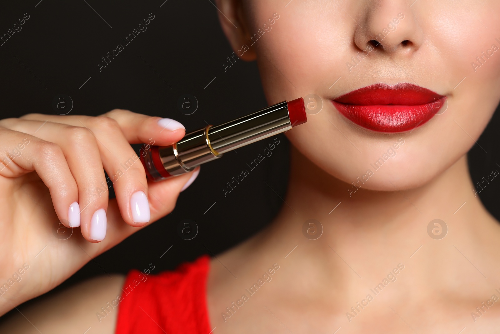 Photo of Young woman with beautiful makeup holding red lipstick on black background, closeup
