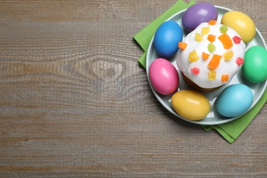 Photo of Traditional decorated Easter cake and colorful eggs on wooden table, top view. Space for text