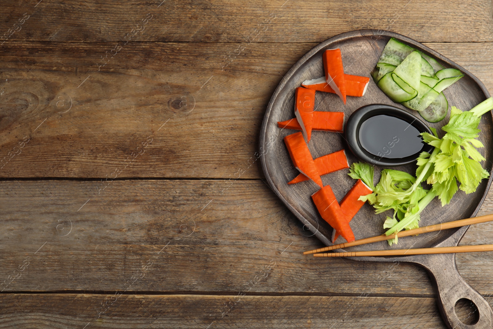 Photo of Fresh crab sticks with lettuce and soy sauce  on wooden table, top view. Space for text