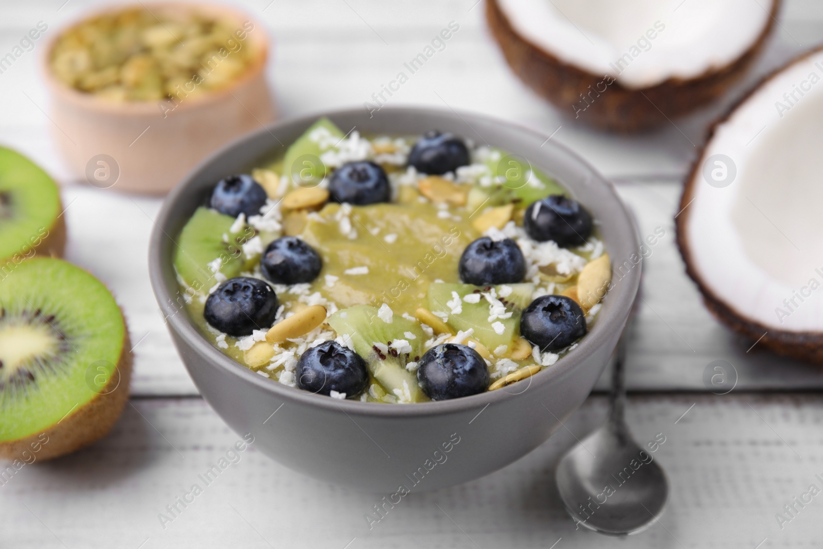 Photo of Bowl of delicious fruit smoothie served with fresh blueberries, kiwi slices and coconut flakes on white wooden table, closeup