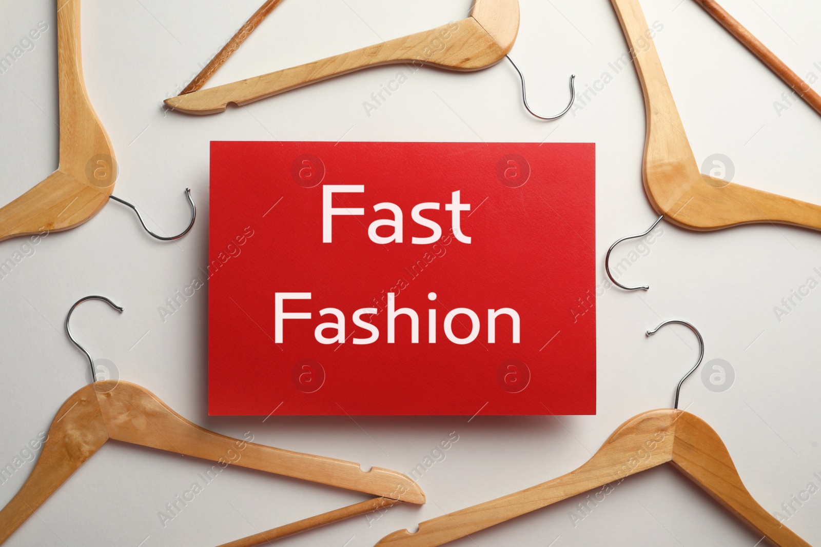 Photo of Red card with phrase Fast Fashion and wooden hangers on white background, top view