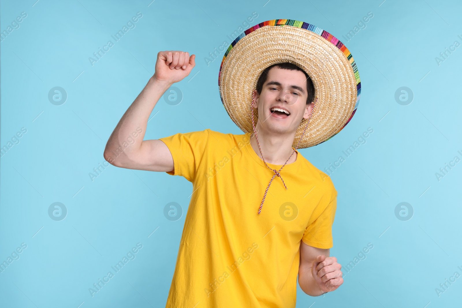 Photo of Young man in Mexican sombrero hat dancing on light blue background