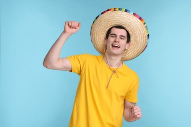 Young man in Mexican sombrero hat dancing on light blue background