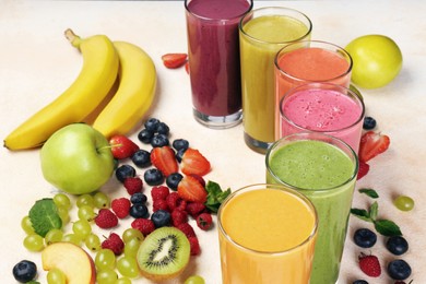 Photo of Fresh colorful fruit smoothies and ingredients on beige table