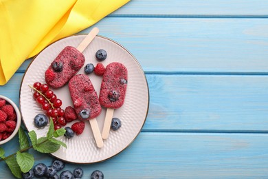 Photo of Plate of tasty fruit ice pops with berries on light blue wooden table, flat lay. Space for text