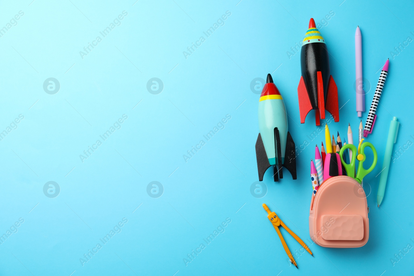 Photo of Bright toy rockets and school supplies on light blue background, flat lay. Space for text