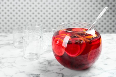 Photo of Bowl of delicious aromatic punch drink, ladle and empty glasses on white marble table. Space for text