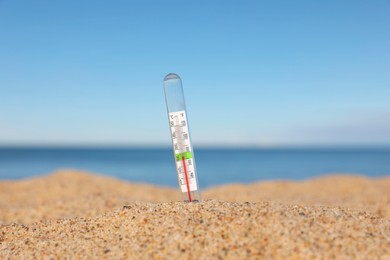 Photo of Glass weather thermometer in sand near sea