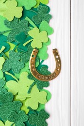 Photo of St. Patrick's day. Golden horseshoe and green decorative clover leaves on white wooden table, flat lay