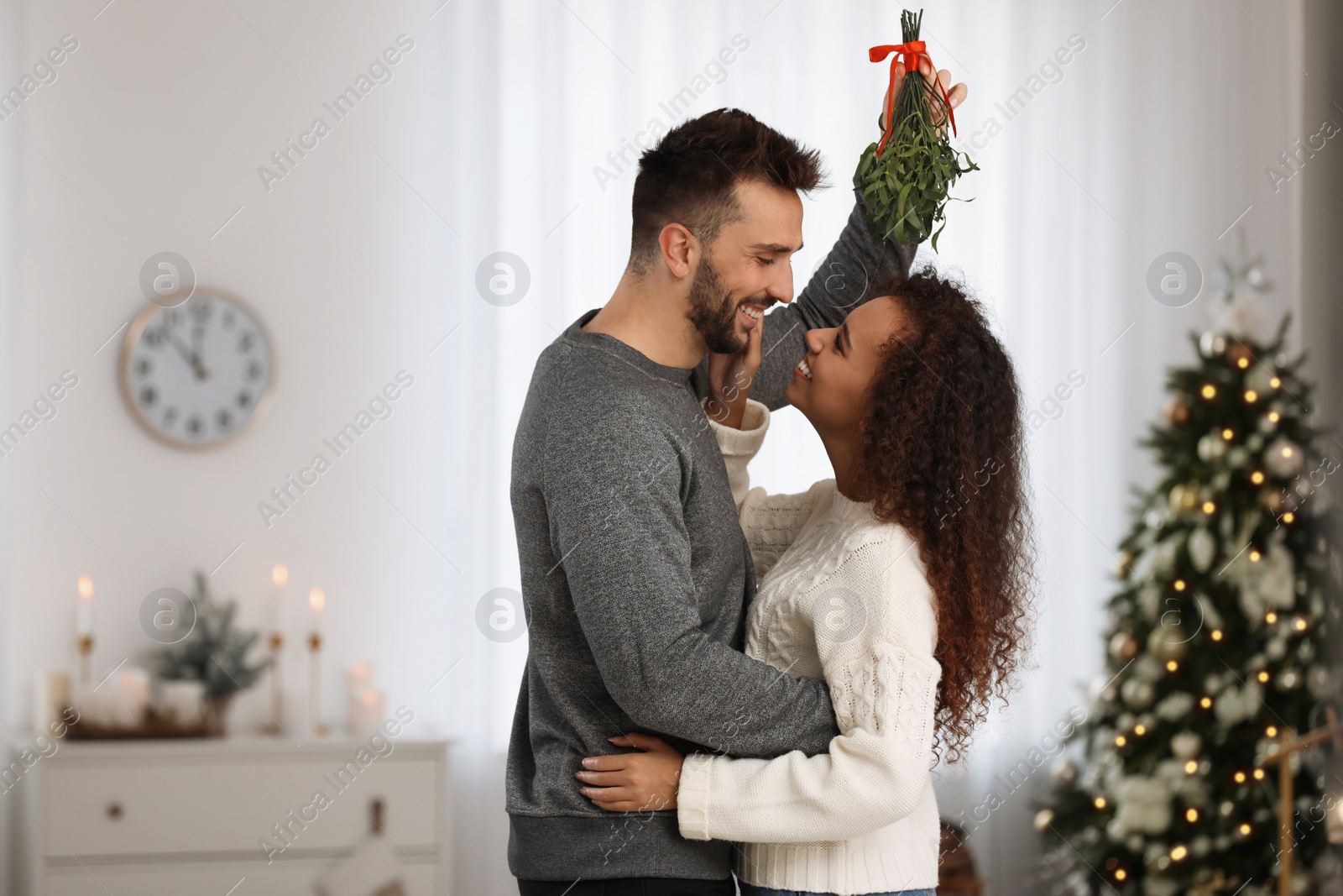 Photo of Lovely couple under mistletoe bunch in room decorated for Christmas