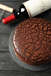 Photo of Delicious chocolate truffle cake, bottle of wine and corkscrew on black wooden table, flat lay