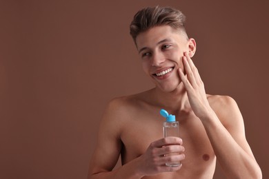 Handsome man applying lotion onto his face on brown background. Space for text