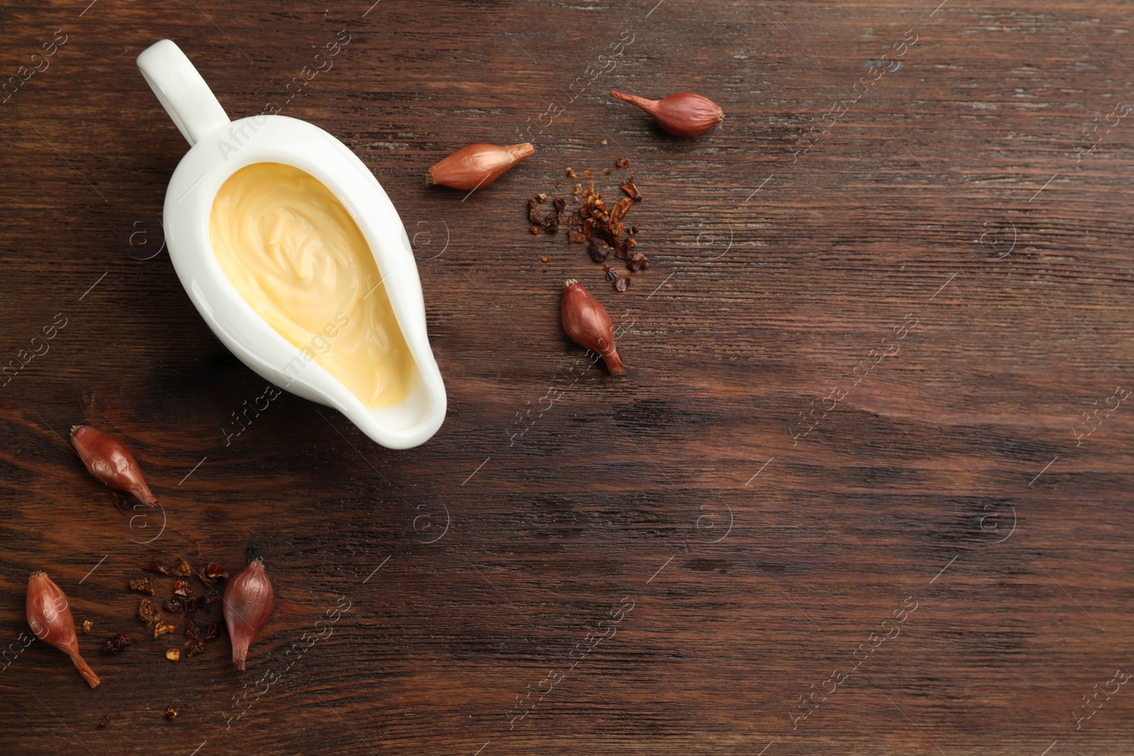 Photo of Tasty sauce in gravy boat, small onion bulbs and spice on wooden table, flat lay. Space for text