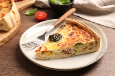 Piece of delicious homemade vegetable quiche and fork on wooden table, closeup
