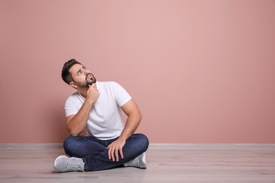 Young man sitting on floor near pink wall indoors. Space for text