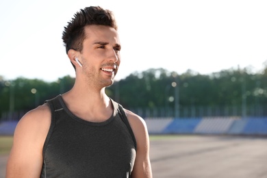 Young sportsman with wireless earphones at stadium