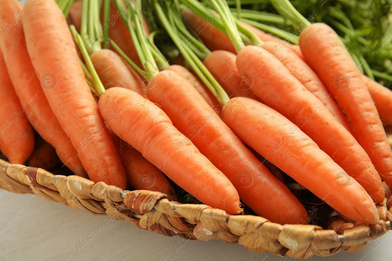 Photo of Wicker tray with ripe carrots on table, closeup