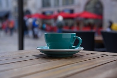 Cup of aromatic hot coffee on wooden table in outdoor cafe