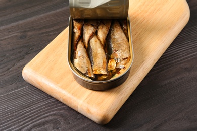 Photo of Board with tin can of sprats on wooden table