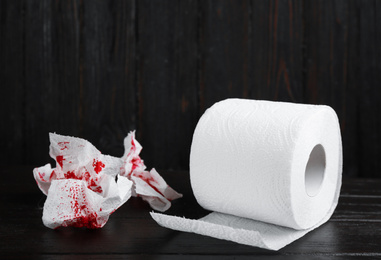 Toilet paper with blood on black wooden table. Hemorrhoid problems