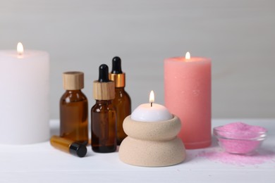 Different aromatherapy products and burning candles on white wooden table, closeup