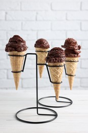 Photo of Chocolate ice cream scoops in wafer cones on white wooden table against brick wall, closeup