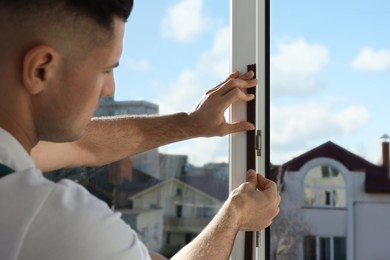 Photo of Man putting rubber draught strip onto window indoors, focus on hands