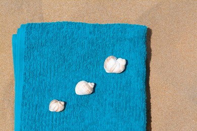 Photo of Folded soft blue beach towel with seashells on sand, flat lay