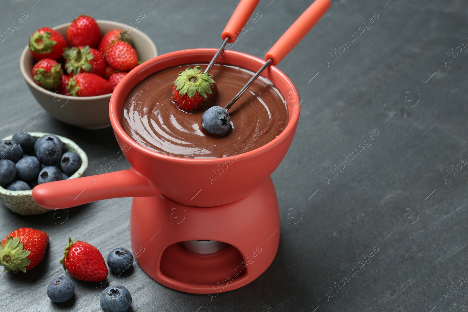 Photo of Dipping fresh berries into fondue pot with melted chocolate at grey table. Space for text