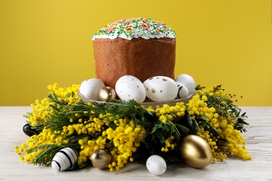 Traditional Easter cake with sprinkles, painted eggs and beautiful spring flowers on white wooden table