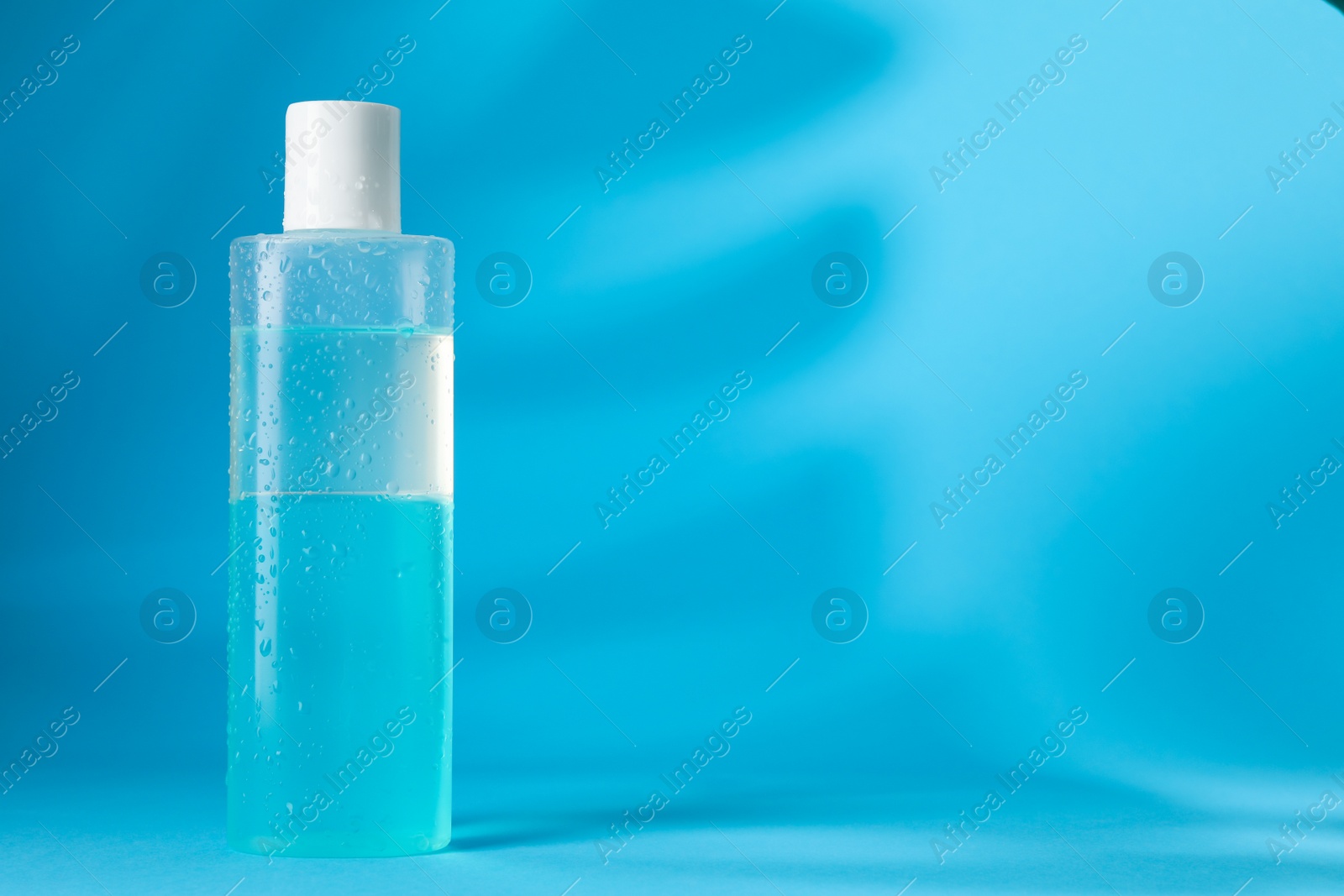 Photo of Wet bottle of micellar water on light blue background, space for text